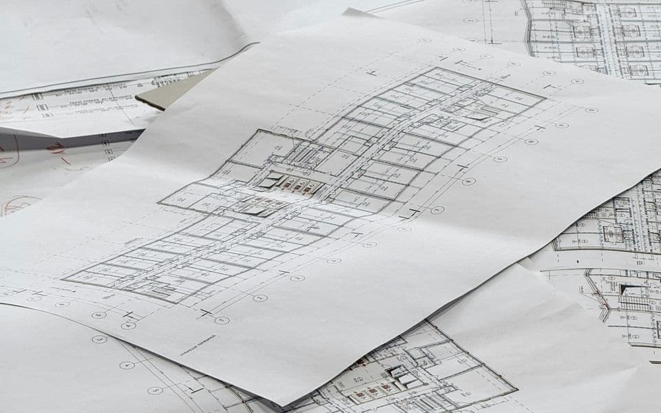 Architectural floor plans and blueprints laid out on a drafting workspace