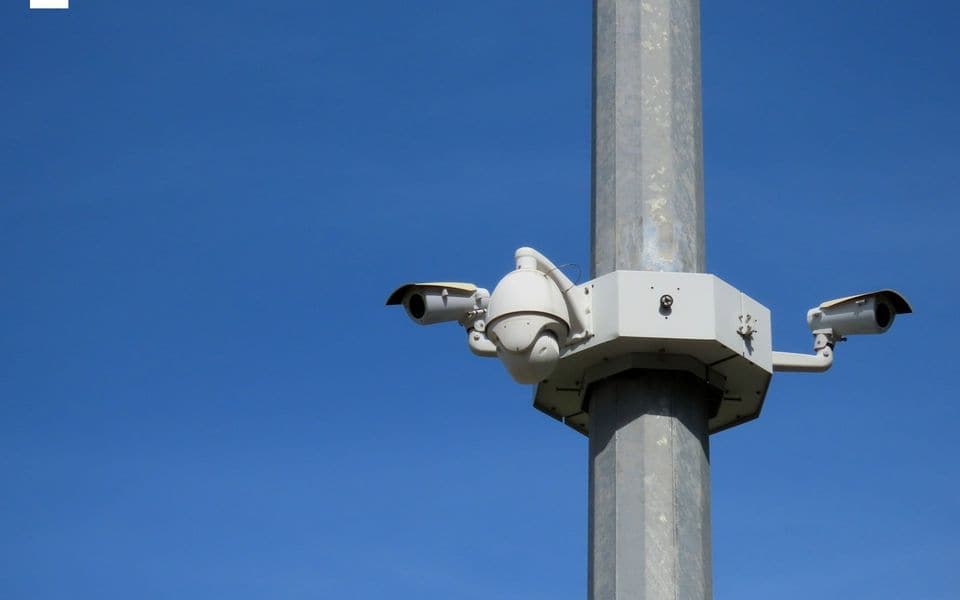 Outdoor security surveillance camera mounted on a galvanized metal pole against blue sky