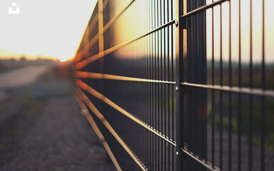 Industrial perimeter metal fence line at golden hour sunset