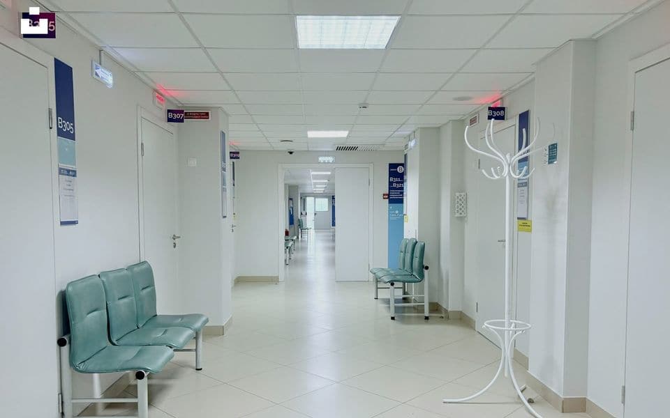 Clean hospital clinic corridor with patient room doors and waiting area benches